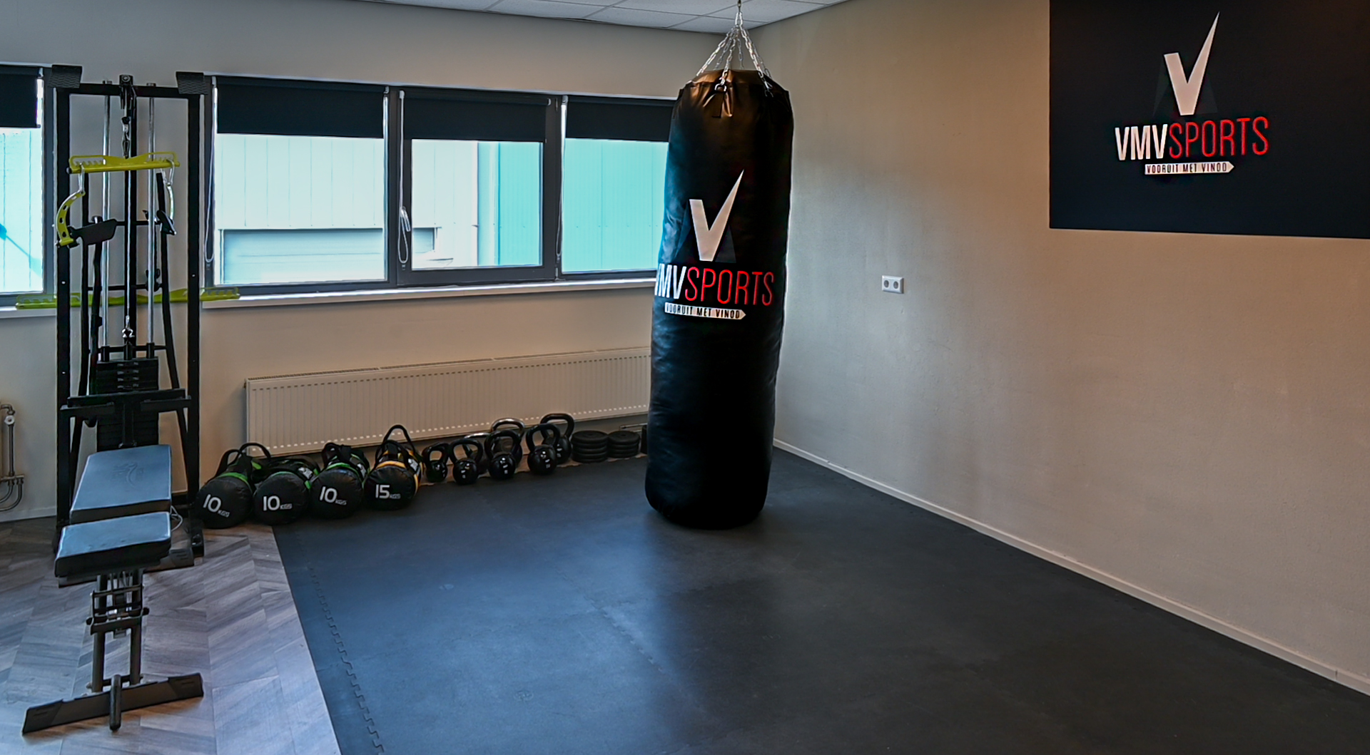 De trainingsruimte van VMV met boxzak, kettlebells, powerbags en een kabelstation onder de ramen
