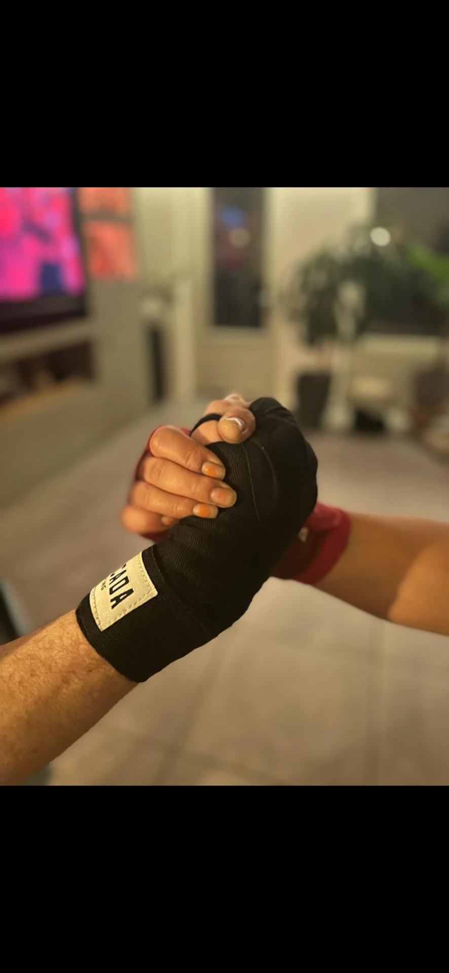 Twee handen met zwarte bokswraps die elkaar vastpakken in de woonkamer, waar VMV begon.